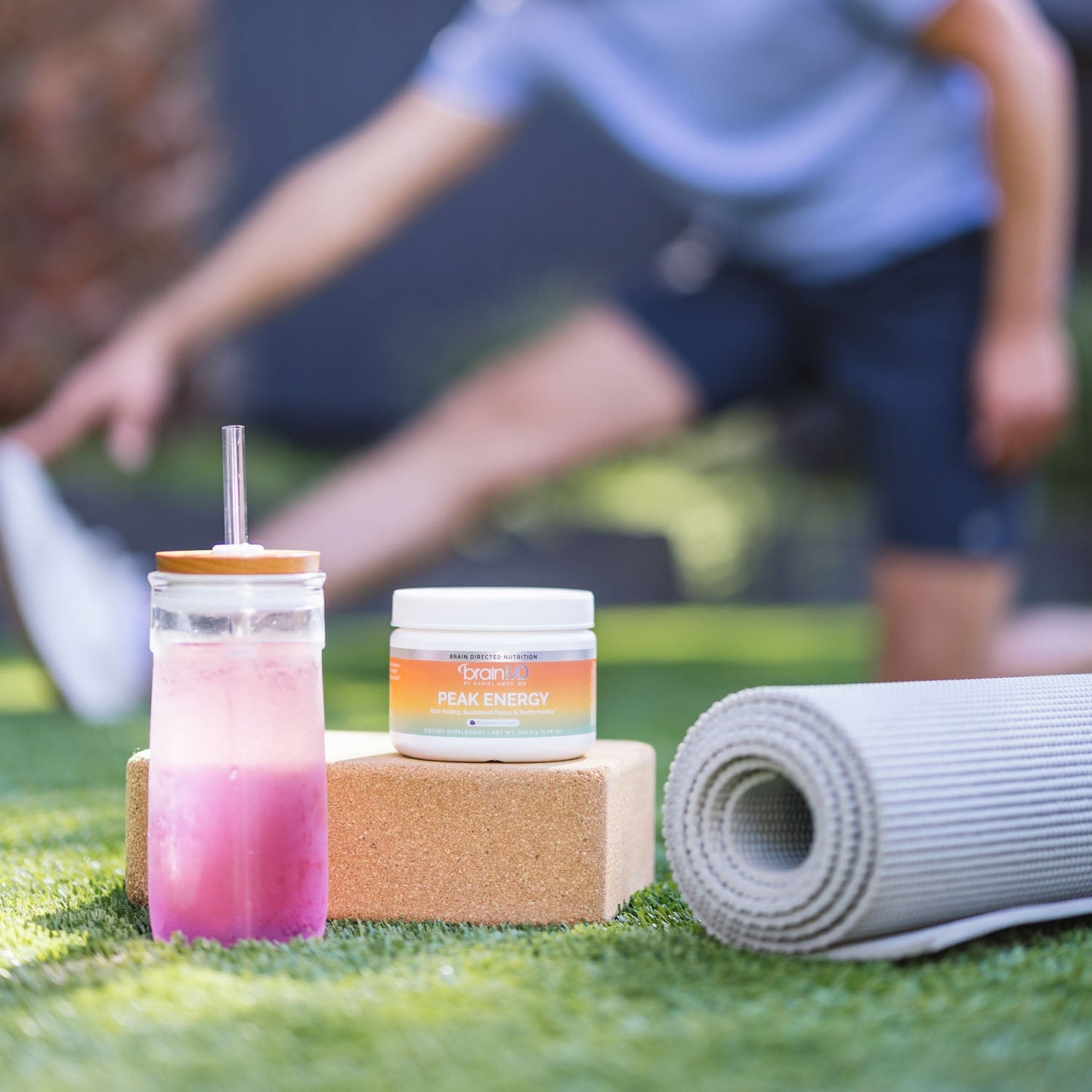 Person stretching in the background with supplement container and drink in the foreground