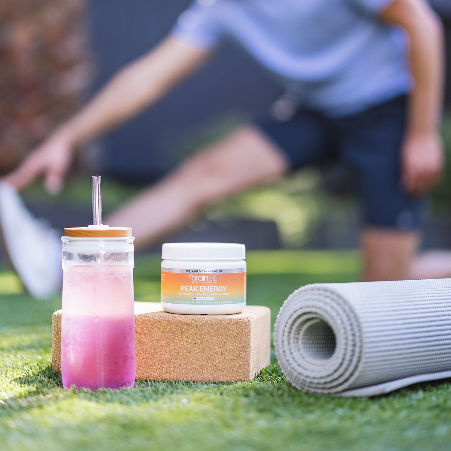 Person stretching in the background with supplement container and drink in the foreground
